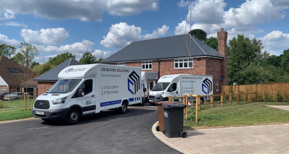 Two CM Moving Solutions removal vans parked outside a red-brick family home on moving day