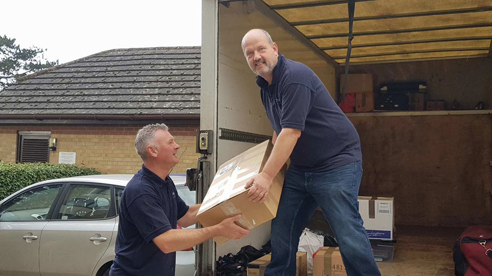 Two members of the CM Moving Solutions team lifting a box into the back of a removal lorry