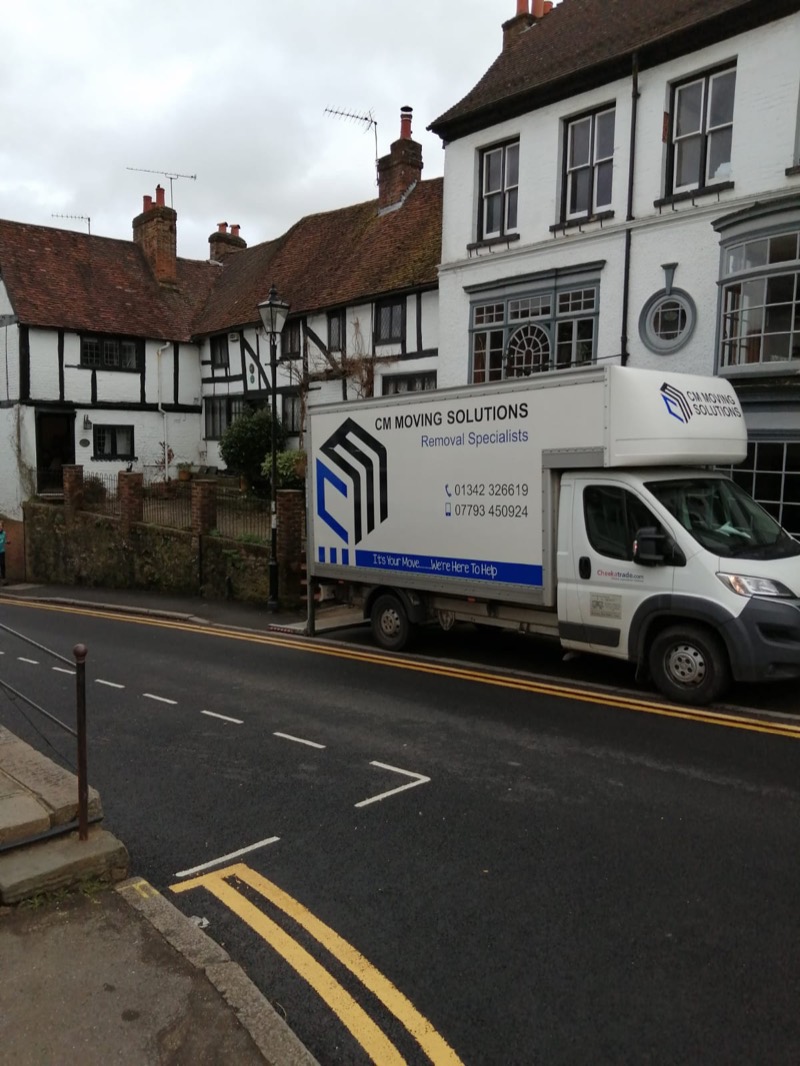 A CM Moving Solutions removal van parked on a historic high street lined with timber-framed buildings
