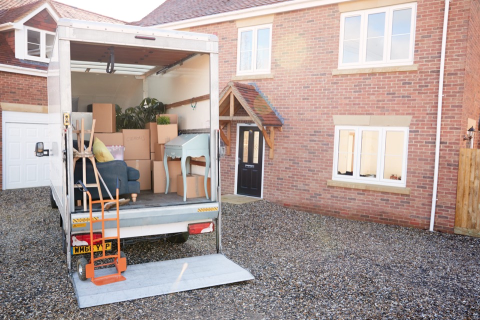 A removal lorry with its tail lift down, loaded with boxes and furniture outside a brick house